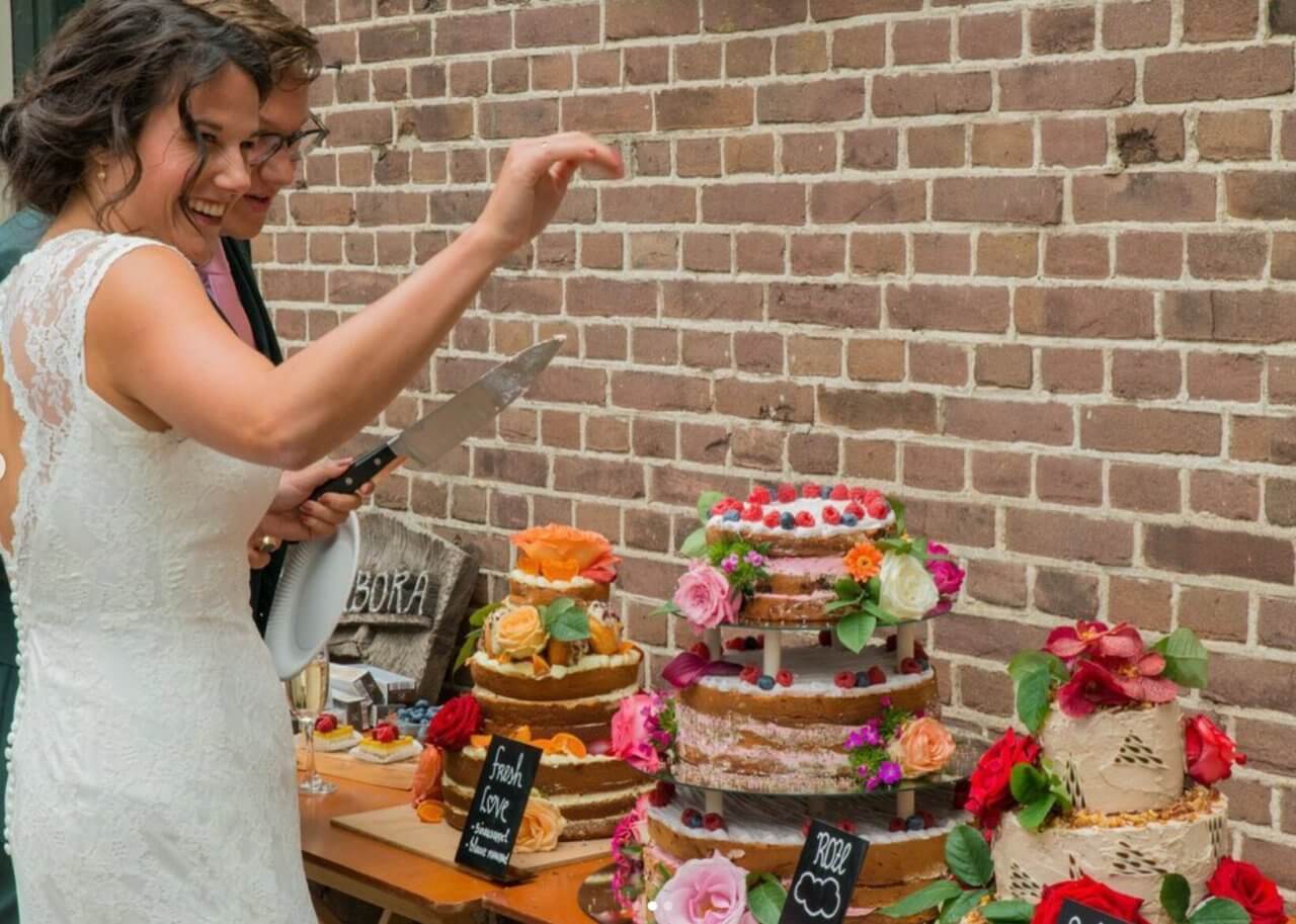 Een stralend bruidspaar staat bij een tafel vol kleurrijke bruidstaarten.