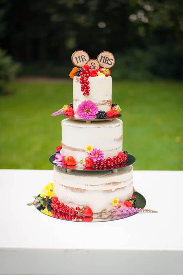 Drie lagen naked cake met witte creme en kleurrijke bloemen.
