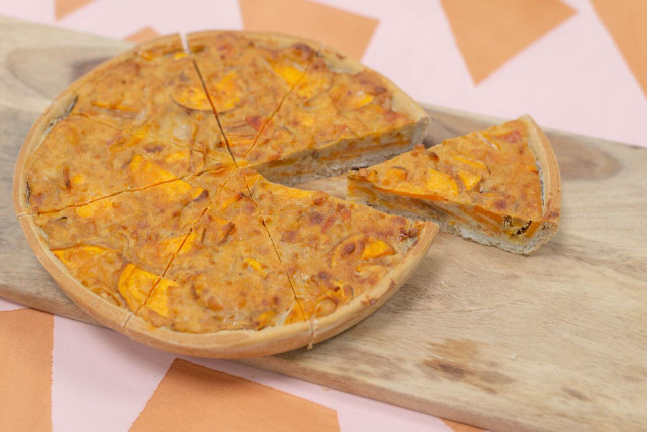 Een vegan quiche van Trashure Taarten, de bakker in Nijmegen, geserveerd op een serveerplank met een stuk eruit gesneden.