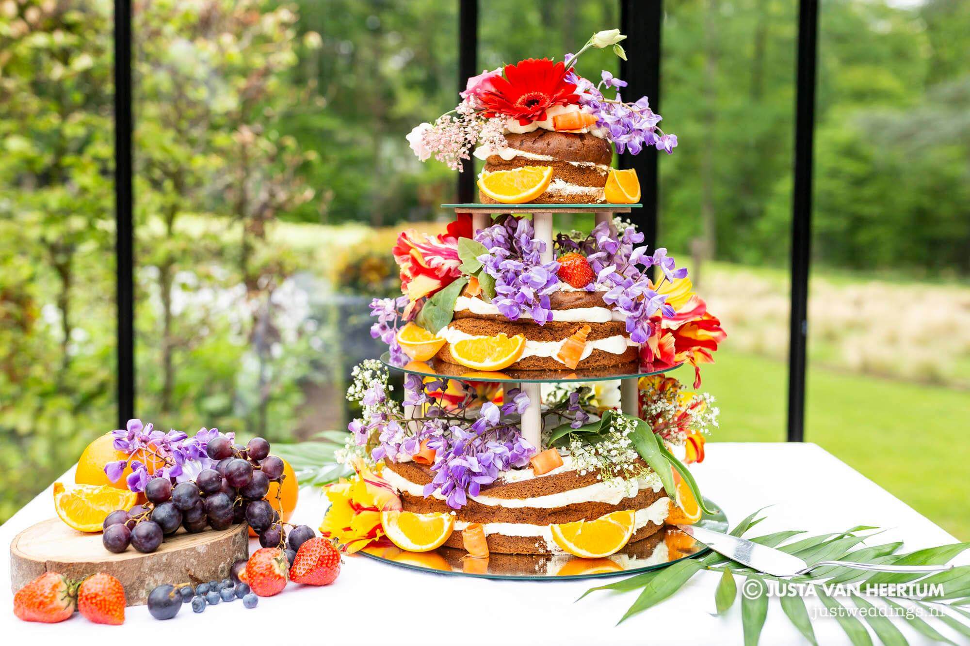 Een rijkelijk versierde bruidstaart met veel kleurrijke bloemen en fruit.