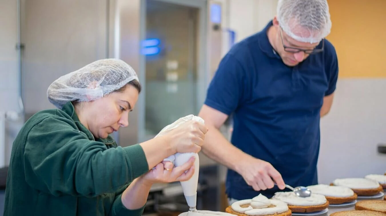 Werknemers in de keuken van Trashure Taarten zijn bezig met het opspuiten van room.